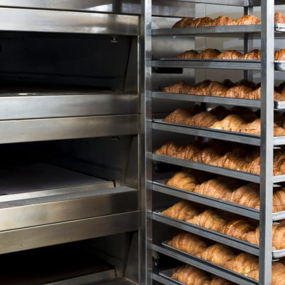 instalación y mantenimiento de hornos industriales en Bogotá” Horno industrial con estantería llena de pan recién horneado en una panadería.